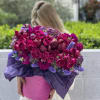 Woman holding a large bouquet of magenta and purple flowers in a pink box