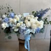 Large blue and white floral arrangement in a white basket with ribbon