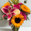 Bouquet of pink roses, sunflowers, and a pink lily in a glass vase