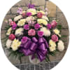 Pink and white floral spray with a purple ribbon bow in a white stand