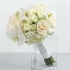 White bridal bouquet of roses, hydrangea, and orchids with ribbon-wrapped stems in a clear glass vase