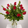 Red roses arranged in a clear glass vase with mixed greenery