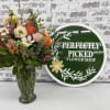 Mixed bouquet of pink, peach, orange, and white flowers in a clear glass vase