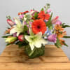 Mixed bouquet with lilies, gerbera daisies, and pastel blooms in a glass vase