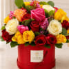 Mixed roses in red, pink, yellow, and white in a red hatbox