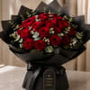 Bouquet of red roses wrapped in black paper with a ribbon and tag