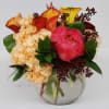 A glass round bowl filled with orange, yellow calla lilies, coral peonies