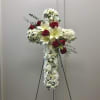 White floral cross arrangement with red roses on a stand