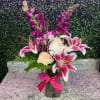 Pink lilies and purple flowers arranged in a glass vase with a ribbon