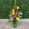Mixed bouquet in a clear glass vase with yellow roses and purple flowers