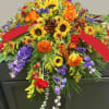 Colorful floral casket spray with sunflowers, orange roses, and purple blooms