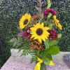 Sunflowers and burgundy flowers in a glass vase with a yellow ribbon
