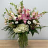 Pink lilies and white blooms arranged in a clear glass vase