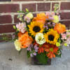 Mixed bouquet with sunflowers, orange roses, and pastel blooms in a glass vase