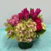 Pink tulips, roses, hydrangea, and orchids arranged in a green vase
