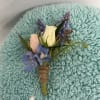 Small boutonniere with a white rose, blue flowers, and purple accents