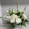 White floral arrangement in a round white vase with lilies and roses