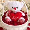 White teddy bear holding a red heart in a basket of rose petals