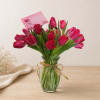 Pink tulips in a clear glass vase with a gold ribbon and card