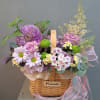 Basket arrangement of pink and purple flowers with a ribbon handle