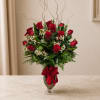 Red roses arranged in a glass vase with a red ribbon