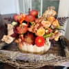 Orange and red floral arrangement in a wooden container with driftwood accents