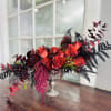 Red roses arranged in a silver pedestal vase with dark foliage
