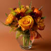 Autumn bouquet of yellow roses and daisies in a clear glass vase with a small pumpkin