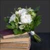White rose bouquet with green accents resting on stacked books