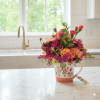Bright pink and orange mixed flower arrangement in a painted floral mug with a butterfly accent.