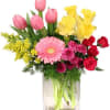Mixed bouquet in a clear glass vase with pink tulips, yellow flowers, and red roses