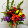 Colorful mixed bouquet in a ribbed vase with red, orange, yellow, and purple blooms