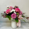 Pink roses and mixed blooms in a white vase with a pink ribbon