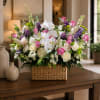 Mixed bouquet in a woven basket with white orchids, pink roses, and purple flowers