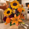 Sunflowers, orange lilies, and marigolds arranged in a square vase