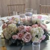 Pink roses and white hydrangeas arranged around glass candle holders on a table