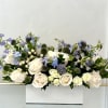 White roses and blue flowers arranged in a white box