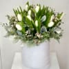 White tulips arranged in a pale round box with greenery