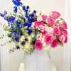 Pink roses and blue flowers arranged in a white vase