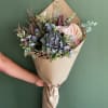Handheld bouquet with anthurium, thistle, and mixed blooms in kraft paper