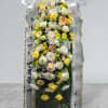 Tall standing floral spray with white ribbon and mixed yellow, white, and peach flowers