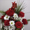 Red roses and white daisies in a festive holiday arrangement with a gift box topper