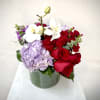 Red roses, lavender hydrangea, and white orchids in a green vase