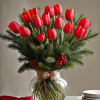 Red tulips arranged in a clear glass vase with evergreen branches and berries