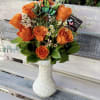 Orange roses arranged in a white vase with small white filler flowers.