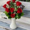 Red roses arranged in a white vase with small white filler flowers.
