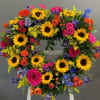 Heart-shaped floral wreath with sunflowers, roses, and blue accents on an easel