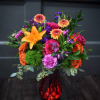 Bright mixed bouquet in a red glass vase with orange, pink, and purple flowers.