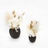 Two dried floral arrangements in dark vases on a white background