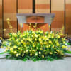 Large low arrangement of yellow lilies and tulips displayed on a stage in front of a podium
